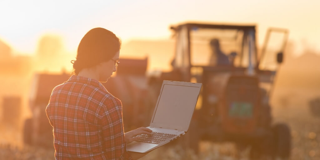 Jovem mulher com laptop em pe no campo representando a Agro Shop