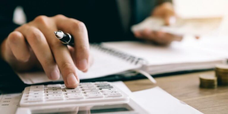 mao usando calculadora e segurando caneta realizando o rateio de custos
